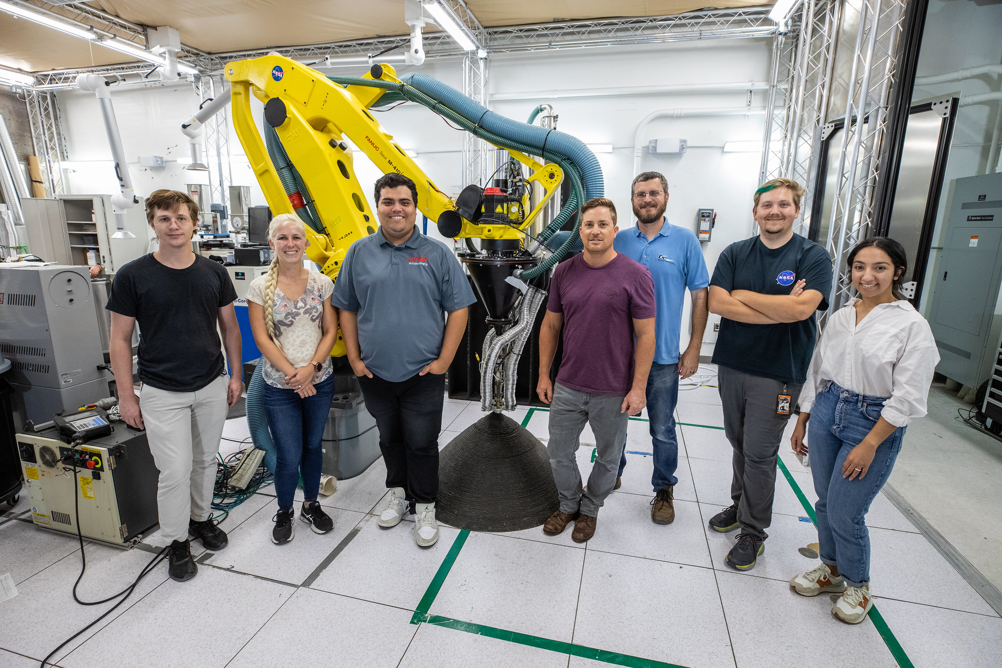 A team at NASA’s Kennedy Space Center in Florida poses with  Zero Launch Mass 3D printer on July 28, 2022, at the Florida spaceport’s Swamp Works, as part of the Relevant Environment Additive Construction Technology (REACT) project.