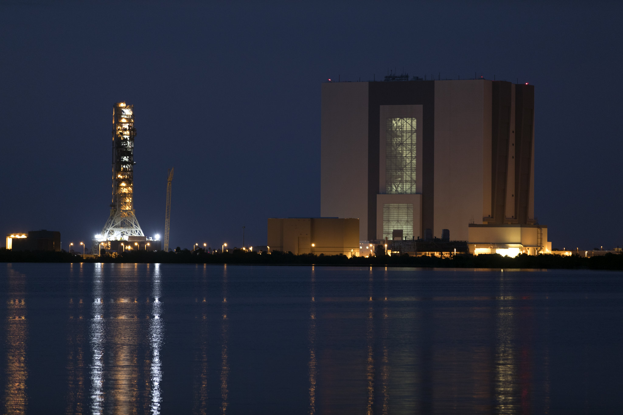 Nighttime view of iconic Vehicle Assembly Building, at right, and mobile launcher at NASA's Kennedy Space Center in Florida, June 21, from  Saturn V center at Kennedy Space Center Visitor Complex. Photo credit: NASA/Kim Shiflett